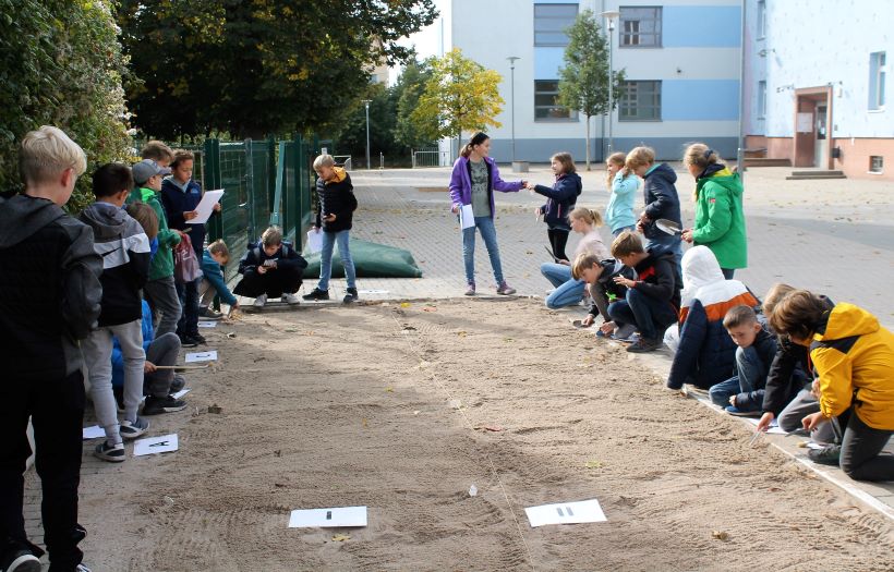 In der Weitsprunggrube auf dem Gelände der Schule sind archäologische Schätze vergraben wurden. Die Schüler:innen beginnen nach Ihnen zu graben.