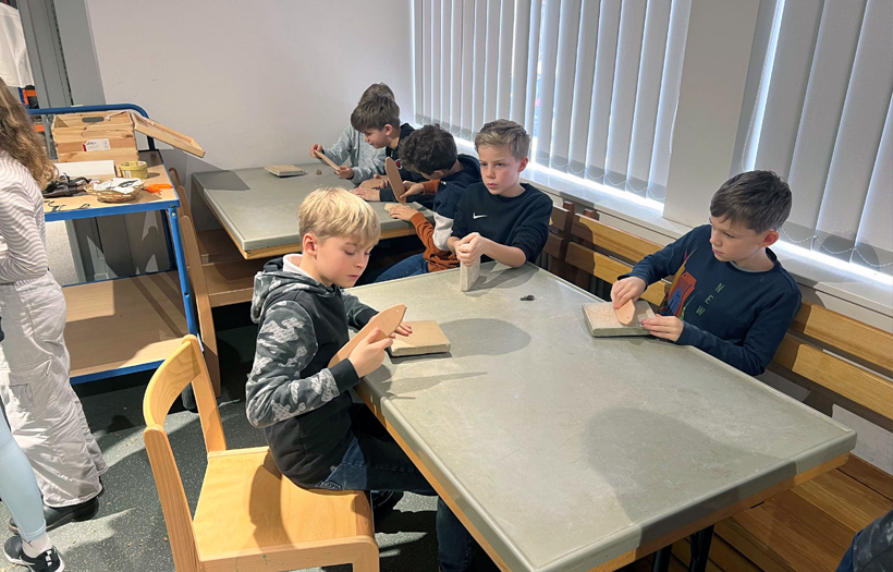 An einem Tisch sitzen Jungen und stellen ihr eigenes Steinzeit-Telefon mit Steinen und Stößeln her.