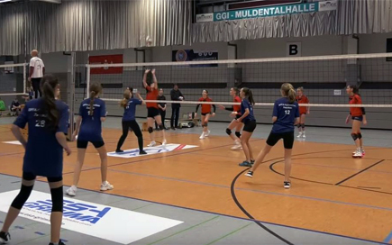In einer großen Sporthalle spielen zwei Volleyballmannschaften gegeneinander.
