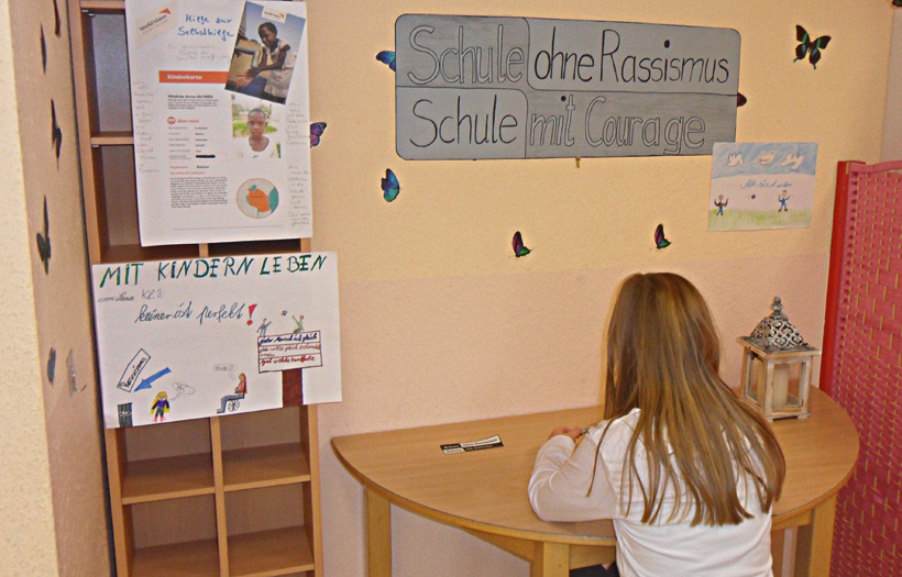 Vor einem selbst gestalteten Bild zum Label "Schule ohne Rassismus" sitzt ein Schulkind an einem tisch.