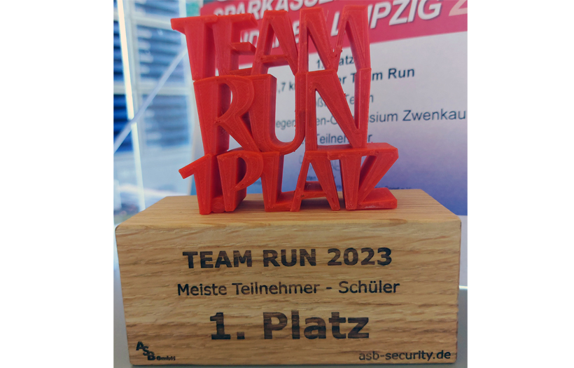 Eine Trophäe im Vordergrund: Auf einem Holzfuß steht in roter Schrift "Team Run 1. Platz".